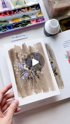 someone is holding an open book with watercolors on it