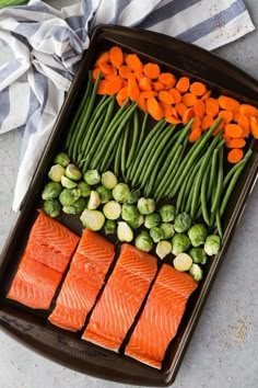 salmon, green beans, and carrots on a baking sheet with other vegetables in the tray