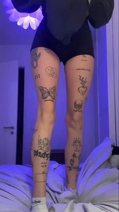 a woman with tattoos on her legs standing on a bed