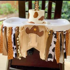 a table topped with a cake covered in brown and white cow print fabric on top of a wooden chair