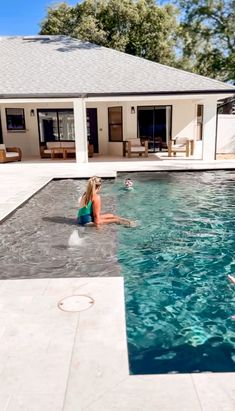 a woman sitting on the edge of a swimming pool in front of a white house