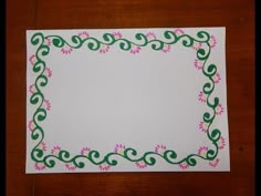 a piece of paper with pink flowers on it and green vines around the edges, sitting on a wooden surface