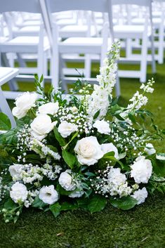 a bouquet of white flowers sitting on top of a grass covered field next to chairs