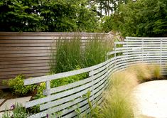 a fenced in area with grass and flowers next to the water feature, surrounded by tall grasses