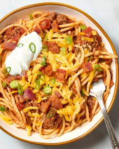 a white bowl filled with pasta and meat topped with sour cream, green onions and bacon