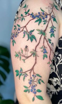 a woman's arm with blue flowers and green leaves on the back of her shoulder