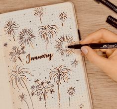 a person writing on a notebook with fireworks in the background and black marker pens next to it