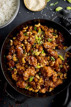 chicken and cashews in a skillet with rice next to it on a black surface