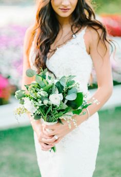 a bride holding a bouquet of greenery in her hands and looking at the camera