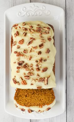 carrot cake with cream cheese frosting and pecans on top, sitting on a white plate