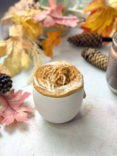 a cappuccino in a white cup on a table surrounded by autumn leaves and pine cones