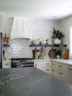 a kitchen with marble counter tops and white cabinets, along with pots on the shelves