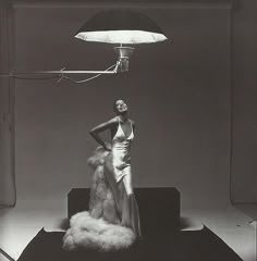 a black and white photo of a woman standing in front of a lamp