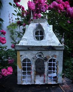 a small house made out of newspaper with pink flowers in the backgroung