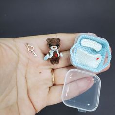 a tiny teddy bear sitting on top of a persons hand next to a key chain