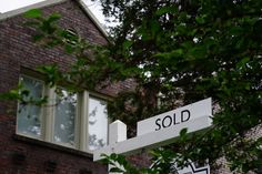 a sold street sign in front of a brick building with trees and bushes around it