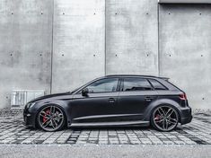 a black car parked in front of a building with red rims on it's tires