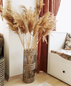 a vase filled with dry grass sitting on top of a floor next to a window