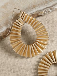 two pairs of gold toned metal earrings on a beige fabric surface with a marble slab in the background