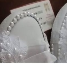 a pair of white shoes with pearls and bows on the front, sitting next to a card