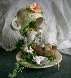 an arrangement of flowers and birds in a teacup on a plate with a lace doily