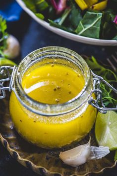 a glass jar filled with yellow liquid sitting on top of a wooden table next to vegetables