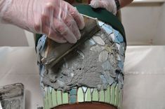 a person in white gloves is working on a vase with blue and green mosaic tiles