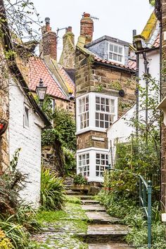 an alley way with stone steps leading up to some buildings and plants on either side