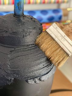 a paintbrush sitting on top of a black pot filled with dark gray paint and brown shaving