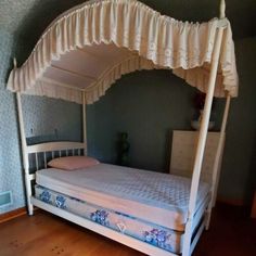 a bed with a white canopy over it on top of a hard wood floor next to a dresser