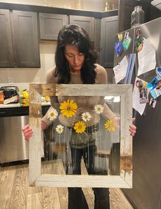 a woman holding up a frame with flowers in it