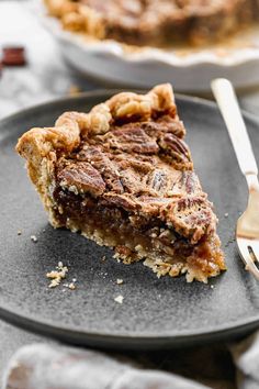 a slice of pecan pie on a black plate with a fork and silverware