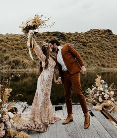 a bride and groom kissing on a dock with flowers in the air next to them