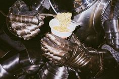 a close up of a person wearing armor eating cereal from a bowl on their hands