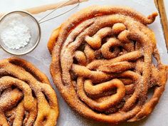 two cinnamon buns sitting on top of a table next to a bowl of powdered sugar