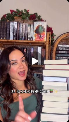 a woman is pointing at a stack of books in front of a bookcase full of books