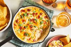 a casserole dish with cheese, bacon and green onions next to some tortilla chips