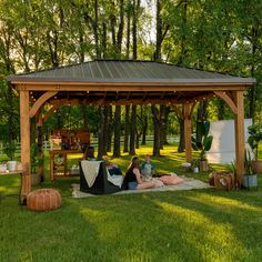 two people sitting on the grass under a wooden gazebo