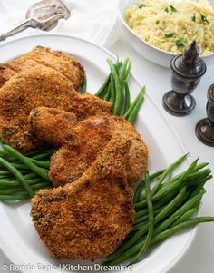 fried chicken with green beans and rice on a white plate next to two silver salt shakers