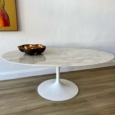 an oval marble table with a bowl on top in front of a white painted wall