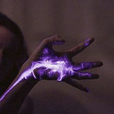 a woman is holding her hand up with purple paint on it and the fingers are glowing