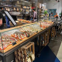 a man standing in front of a counter filled with lots of different types of pizza