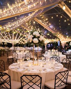 a large tent with tables and chairs set up for a formal dinner or party under string lights