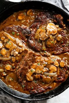 two steaks with mushrooms and onions in a cast iron skillet on a marble surface