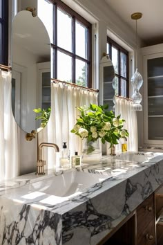 a bathroom with marble counter tops and two mirrors on the wall, along with vases filled with flowers