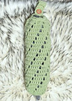 a green crocheted bottle cover laying on top of a fur rug with a button in the middle