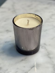 a candle sitting on top of a white marble counter next to a black and silver cup