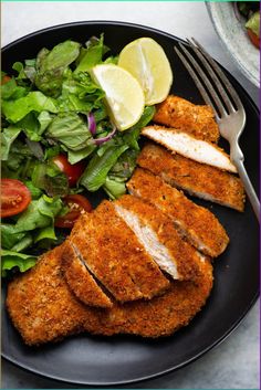 a plate with chicken, salad and lemon wedges on it next to a fork