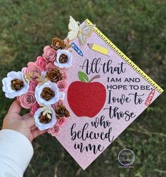 a hand holding up a pink graduation cap with flowers on it that says, all that i am and hope to be