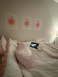 an unmade bed with two pictures on the wall above it and a laptop computer